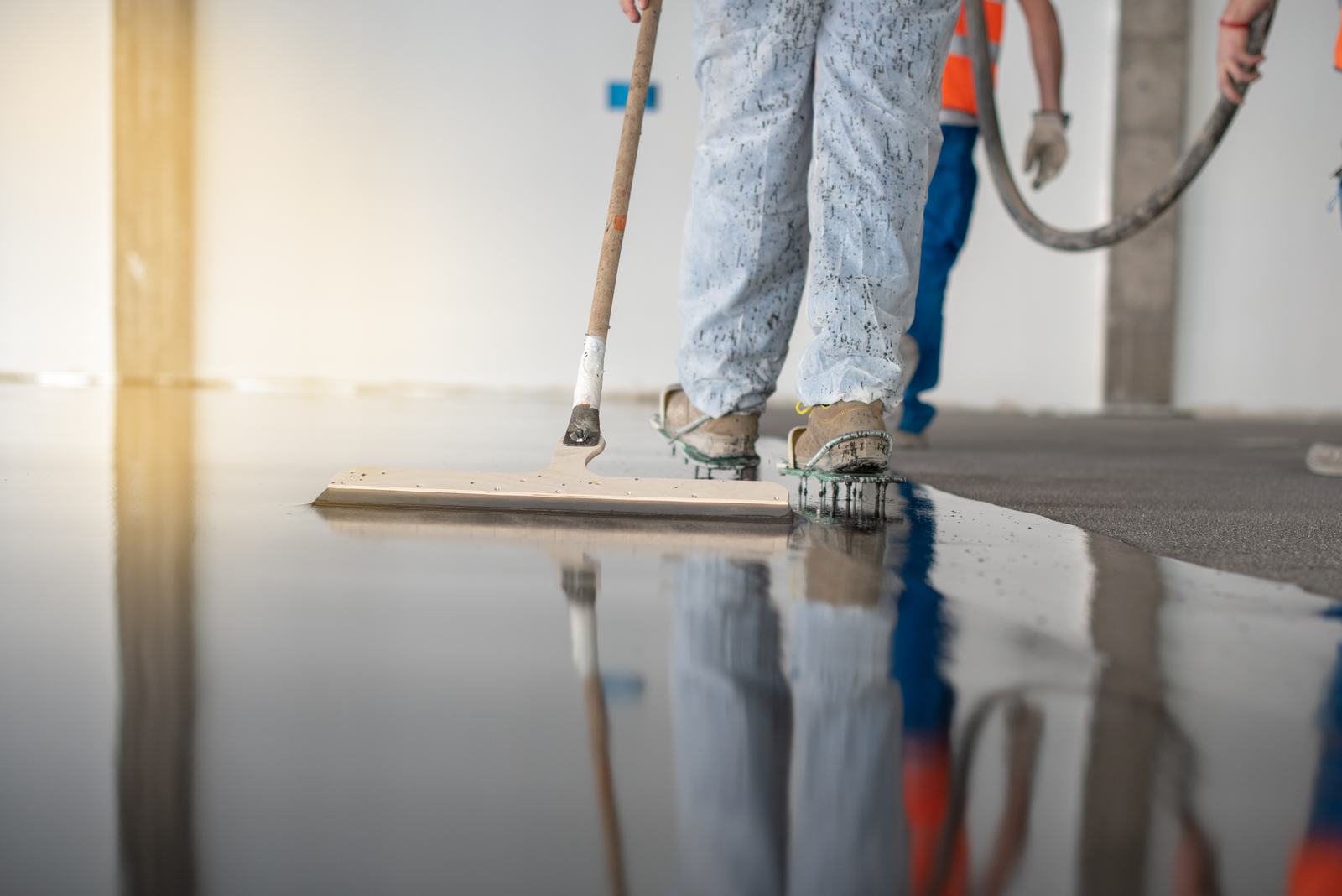 Crew leveling a fresh glossy floor coating with a squeegee while wearing spiked shoes